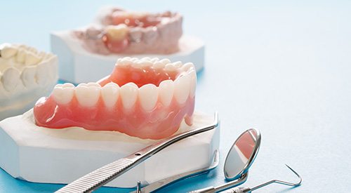 Model of denture next to dental tools