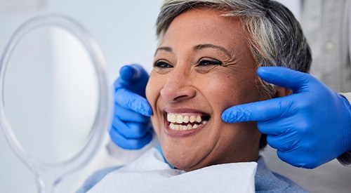 Woman smiling at reflection in handheld mirror