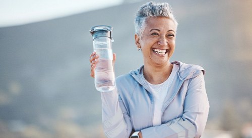 Woman smiling with water bottle on hike outside