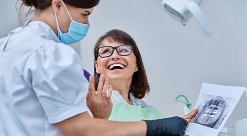 Woman smiling with dentist while reviewing X-ray