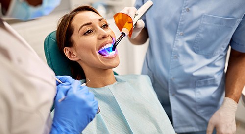 Dentists applying UV light to woman’s dental bonding