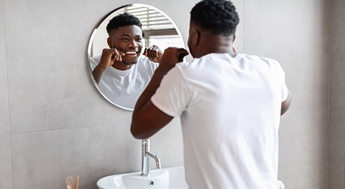 Man smiling while flossing in mirror