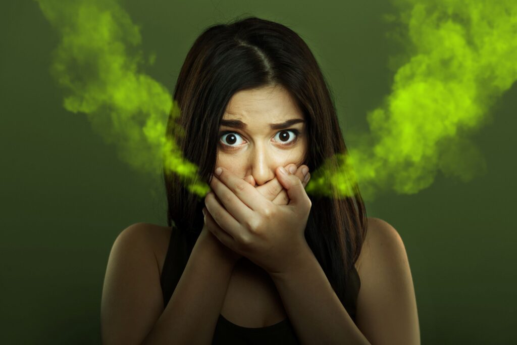 Woman with brown hair holding hands over mouth with stinky green smoke pouring out